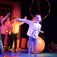 "Ava auf der Zirkusbühne mit einem Arm zur Seite gestreckt"