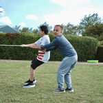 Zwei Jungen spielen gemeinsam im Freien und halten lachend ein Seil - ein Moment von Bewegung, Freude und gemeinschaftlicher Teilhabe auf einer gruenen Wiese.