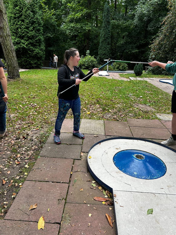 "Maya berührt beim Minigolfen mit ihrem Schläger mit einem anderen Schläger."